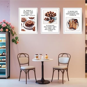Pode incluir: Três impressões de sobremesas emolduradas com bordas brancas penduradas em uma parede rosa. As impressões apresentam ilustrações em aquarela de sobremesas de chocolate e texto. Uma pequena mesa com duas cadeiras está em frente à parede.