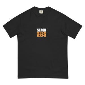 Puede incluir: Camiseta negra con la palabra "STACK" en letras blancas sobre tres líneas de "SATS" en naranja. La camiseta es de estilo cuello redondo.