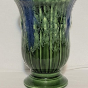 Könnte beinhalten: Eine grün-blaue Keramikvase mit Sockel. Die Vase hat einen ausgestellten Rand und ein strukturiertes, vertikales Muster. Die Farben verschmelzen, mit Blau oben und Grün im Rest der Vase.
