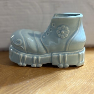 Könnte beinhalten: Hellblauer Keramik-Blumentopf in Stiefelform. Der Stiefel hat dekorative Nähte, ein Blumendetail und eine dicke Sohle. Dieser Pflanztopf ist für kleine Pflanzen oder Blumen konzipiert und verleiht der Inneneinrichtung eine einzigartige Note.