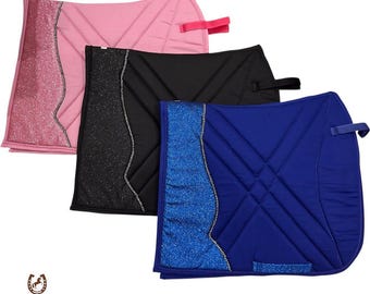 May include: Three equestrian saddle pads in pink, black, and blue. Each pad features a glittery accent panel and a quilted design. The pink pad has a pink strap, the black pad has a black strap, and the blue pad has a blue strap.