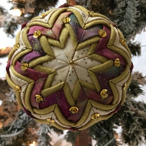 Könnte beinhalten: Ein handgefertigter Weihnachtsbaumschmuck mit Sternmuster. Der Schmuck besteht aus Stoffen in Creme, Burgunderrot und Gold, verziert mit goldenen Pailletten. Er hängt an einem goldenen Faden, ideal für die Weihnachtszeit.