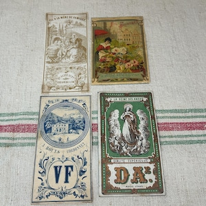 May include: Four rectangular vintage paper labels featuring intricate illustrations. One shows a family scene, another a flower market, a third a blue mountain landscape with the letters VF, and the fourth a religious figure with the letters DA.