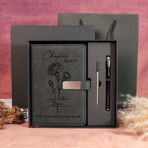 May include: A dark grey journal and pen set in a gift box. The journal features the text "Chapter Thirty", a floral design, and the name "Diana". The set includes a pen and a refill, presented in a matching gift box.