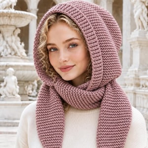 May include: A dusty rose knitted hooded scarf featuring a textured garter stitch pattern. The accessory consists of a deep hood that transitions into two long, pointed ends that drape down the front, providing full coverage for the head and neck.