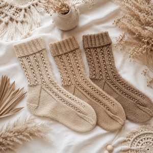 Puede incluir: Tres pares de calcetines de punto en tonos variados de beige, bronceado y marrón. Cada calcetín presenta un puño acanalado en la parte superior, un patrón de trenzas verticales a lo largo de la pierna y el pie, y una sección lisa en el talón y la punta.