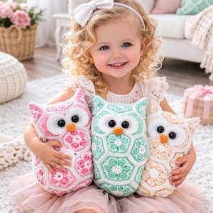May include: A smiling child holds three crochet owl cushions. The owls are pink, mint green, and cream, with black eyes and orange beaks. The child wears a white headband and a pink tutu. The cushions are handmade.