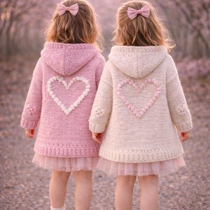 Peut inclure: Deux enfants portant des manteaux à capuche roses et crème assortis avec des motifs de cœur dans le dos. Elles portent également des jupes en tulle roses, des chaussettes blanches et des chaussures beiges. Le fond est une scène extérieure floue rose et verte.
