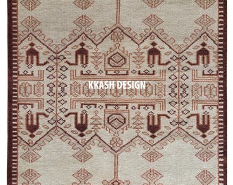 Op de afbeelding: Rechthoekig tapijt met een beige en bruin geometrisch patroon. Het tapijt heeft herhaalde ruit-, driehoek- en gestileerde figuurmotieven. De tekst "KKASH DESIGN" is zichtbaar in het midden van het tapijt.