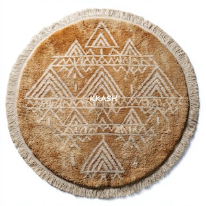 May include: Round, tan rug with a geometric white design and fringe trim. The rug features a repeating pattern of triangles and other shapes. The text "KKASH" is printed in the center of the rug.