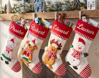 Puede incluir: Cuatro calcetines navideños blancos con puños rojos que llevan los nombres Phoebe, Robert, Edward y Lauren. Cada calcetín muestra un personaje de peluche: un gato, un perro, un reno y un muñeco de nieve, todos con bufandas y gorros a rayas rojas y blancas.