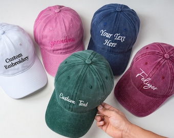 Puede incluir: Cinco gorras de béisbol en blanco, rosa, azul oscuro, verde oscuro y granate. Cada gorra presenta texto bordado en la parte frontal: Custom Embroidery, grandma, Your Text Here, Custom Text y Feliyer. Tienen corona estructurada y visera.