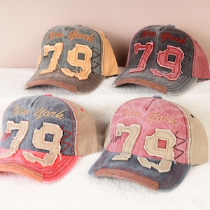 Pode incluir: Quatro bonés de beisebol com um visual desgastado. Cada boné tem "New York" bordado acima do número "79". Os bonés são em várias cores, incluindo vermelho, cinza e bege, com uma aparência vintage.