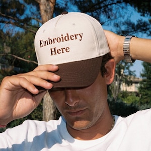 Puede incluir: Una gorra de b&eacute;isbol bicolor con una corona de color crema y una visera de color marr&oacute;n oscuro. La parte delantera de la corona muestra el texto Embroidery Here bordado en hilo marr&oacute;n oscuro. La gorra tiene un dise&ntilde;o estructurado de cinco paneles.