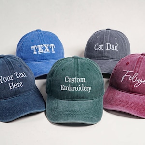 May include: Five baseball caps in blue, dark blue, green, grey, and maroon with white embroidered text. The caps feature the phrases TEXT, Your Text Here, Custom Embroidery, Cat Dad, and Feliyer in various fonts on the front panels.