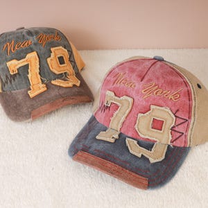 May include: Two baseball caps with a vintage look. One is gray and yellow, the other is red and blue. Both caps feature the text "New York" and the number "79" in a distressed style.