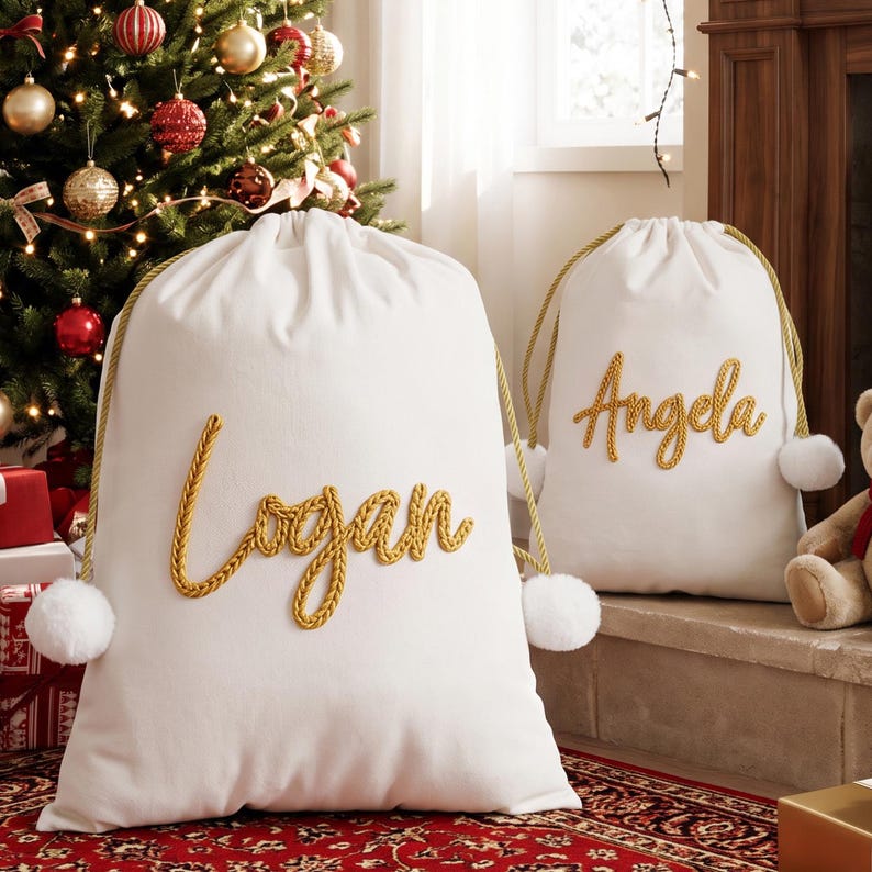 May include: Two white fabric drawstring bags featuring gold rope lettering that spells out the names Logan and Angela. Each bag includes gold rope drawstrings and white pom-pom accents at the base of the closure on both sides.