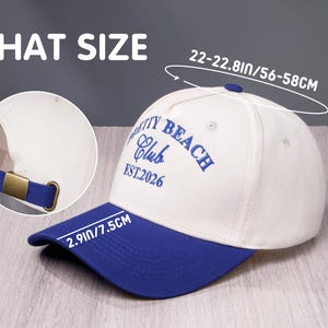 Puede incluir: Una gorra de b&eacute;isbol blanca y azul con el texto bordado PRETTY BEACH Club EST.2026. La gorra tiene una visera azul, una hebilla ajustable color lat&oacute;n y unas dimensiones de 56-58cm de circunferencia, 14,5cm de altura y 7,5cm de visera.