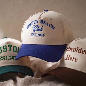 Puede incluir: Tres gorras de b&eacute;isbol con coronas de color crema y viseras en contraste. La gorra central tiene una visera azul y el texto azul PRETTY BEACH Club EST.2026. La gorra izquierda tiene una visera verde y el texto verde CUSTOM EST.2026. La gorra derecha tiene una visera marr&oacute;n y el texto marr&oacute;n Embroidery Here.