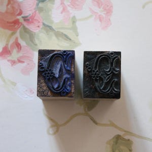 May include: Two rectangular wooden stamps with floral designs. One stamp has a dark blue floral pattern, while the other has a black floral pattern. The stamps are on a light-colored surface with floral patterns.