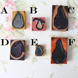 Puede incluir: Colección de seis sellos de madera con forma de pera. Cada sello presenta un diseño de pera negra montado sobre un bloque de madera rectangular. Los bloques tienen varios colores de fondo, incluyendo amarillo y naranja.