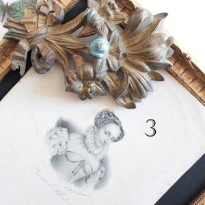 Puede incluir: Marco de fotos antiguo dorado y ornamentado con interior negro. El marco presenta un diseño floral y de cinta detallado en la parte superior. Un retrato en blanco y negro de una mujer es visible dentro del marco. El número 3 está impreso en la imagen.