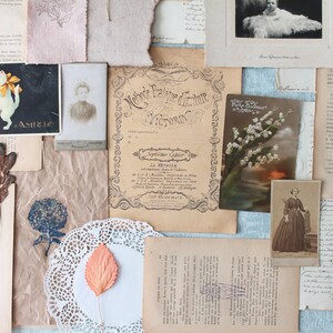 May include: A collage of vintage ephemera, including old book pages, postcards, and photographs. The items are arranged on a light blue surface. Notable elements include a postcard with two cats, a dried leaf, and a vintage document.