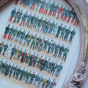 Puede incluir: Una impresión antigua titulada "UNIFORMES" que presenta varias ilustraciones de uniformes militares y formales. La impresión está enmarcada en un marco ovalado de madera envejecida, teñido de rosa, con adornos florales.