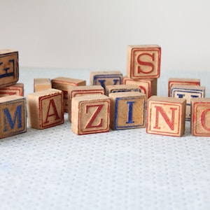 May include: Wooden alphabet blocks spelling the word "AMAZING". The blocks are a light brown colour with red and blue letters. The blocks are arranged on a light blue surface.