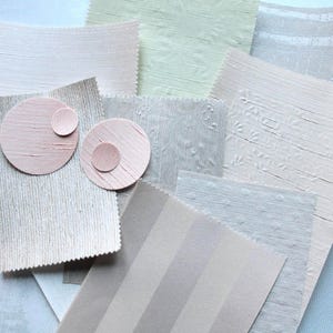 May include: A collection of fabric swatches in pastel shades of pink, beige, and grey. The samples feature diverse patterns, including stripes, floral, and solid textures. Two pink painted circles with smaller circles are also present.