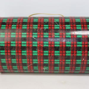 May include: A cylindrical tin with a red, black, and green plaid pattern. The tin has a beige handle and a metallic rim. The plaid design is a classic pattern, and the tin appears to be vintage.