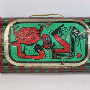 May include: Vintage metal lunchbox with a green, red, and black plaid pattern. The front features a cartoon illustration of a girl with red hair and a small creature. The lunchbox has a yellow handle and a metal clasp.