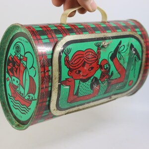 May include: Vintage metal lunchbox with a red and green plaid pattern. The ends feature a green background with a red sailboat illustration. The front has a cartoon girl and a monkey. Includes a white handle.