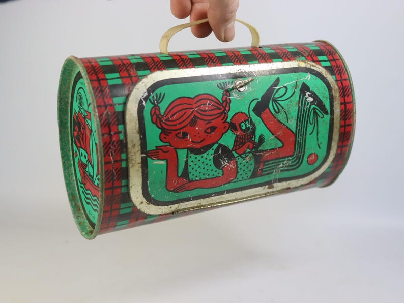 May include: Vintage metal lunchbox with a red and green plaid pattern on the sides. The front features a cartoon girl with red hair and a monkey on a green background. It has a yellow plastic handle.
