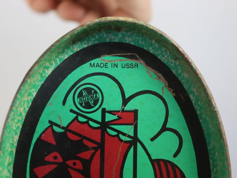 May include: Vintage oval metal tray with a green background and a black and red graphic of a ship. The tray has the text "MADE IN USSR" and a logo that says "NORMA". The tray has a distressed look.