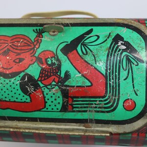 May include: Vintage metal lunchbox with a green and red plaid pattern. The lid features a cartoon girl with red hair and a monkey, set against a green background. The lunchbox has a metal handle and a latch closure.