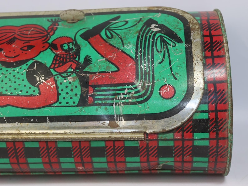 May include: Vintage metal lunchbox with a green, red, and black plaid pattern. The lid features a cartoon illustration of a girl with a monkey, in red and black on a green background. The lunchbox has a silver metal clasp.
