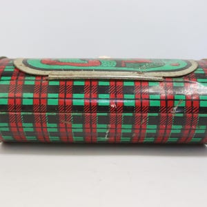 May include: A vintage, cylindrical tin box with a plaid pattern in red, green, and black. The lid features a green and red design. The metal box has a clasp closure and is likely used for storage or as a decorative item.
