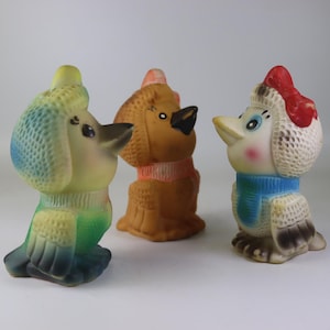 May include: Three vintage rubber animal toys: a poodle, a dog, and a bird. The poodle is yellow, green, and blue. The dog is brown with an orange collar. The bird is white, red, and blue.