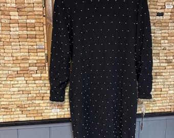May include: A black, long-sleeved dress with white polka dots and a decorative collar. The dress is hanging on a black hanger against a wooden background.