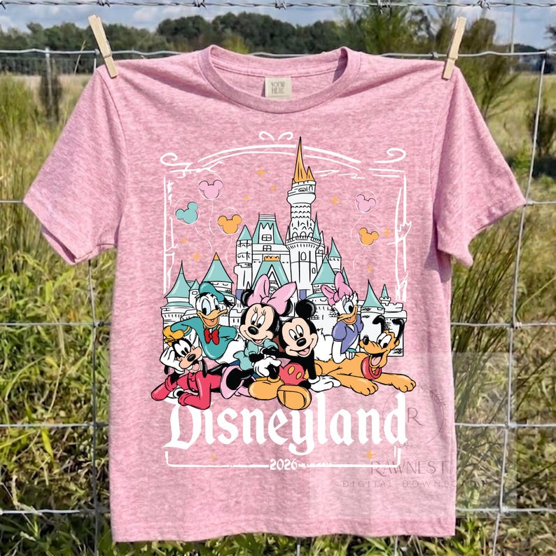Peut inclure: Un t-shirt &agrave; manches courtes rose chin&eacute; avec une impression graphique repr&eacute;sentant un ch&acirc;teau et des personnages Disney dont Mickey, Minnie, Donald, Daisy, Dingo et Pluto. Le texte Disneyland 2026 est imprim&eacute; sous les personnages.