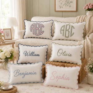 May include: Six rectangular white throw pillows with scalloped edges. Two pillows feature embroidered monograms in pink and green gingham. Four pillows are embroidered with the names William, Olivia, Benjamin, and Sophia in various colors.