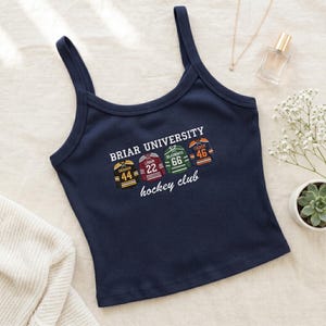 Könnte beinhalten: Marineblaues Tanktop mit Spaghettiträgern. Das Oberteil zeigt den Text "Briar University hockey club" und vier Hockey-Trikot-Designs mit Spielernamen und -nummern: Graham 44, Logan 22, Delaurentis 66 und Tucker 46.