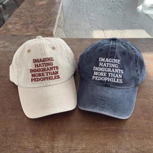 Può includere: Due cappellini da baseball, uno color crema e uno blu navy, sono esposti. Entrambi i cappellini presentano la scritta ricamata "IMAGINE HATING IMMIGRANTS MORE THAN PEDOPHILES". I cappellini sono su una superficie di legno.
