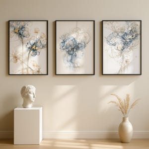 Op de afbeelding: Drie ingelijste wandkunstwerken met abstracte blauwe en gouden bloemen- en menselijke profielillustraties. Daaronder staat een wit borstbeeld op een voetstuk en een beige vaas met gedroogd pampasgras voor een samenhangend geheel.
