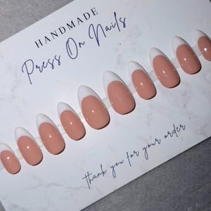 Könnte beinhalten: Ein Set handgefertigter Press-On-Nägel mit klassischem French-Maniküre-Design. Die Nägel haben eine nude Basis mit weißen Spitzen. Die Karte lautet "HANDMADE Press On Nails" und "thank you for your order".