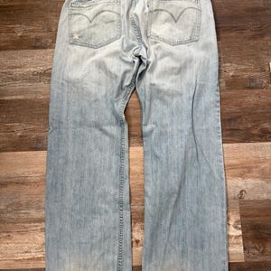 May include: Pale blue denim jeans with a faded appearance. The jeans feature a classic five-pocket design, a button and zip fastening, and the Levi's logo on the back pockets. The jeans show signs of wear and tear.