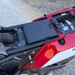 Può includere: Primo piano di una moto Yamaha rossa e bianca. La sella è aperta, rivelando i componenti del motore e un vano portaoggetti nero. La chiave della moto è nel contatto.