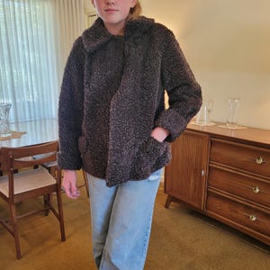 Peut inclure: Veste marron foncé texturée avec un grand col et des poches. La veste est faite d'une matière douce et floue. Les manches sont retroussées aux poignets. La veste est portée sur un jean bleu.