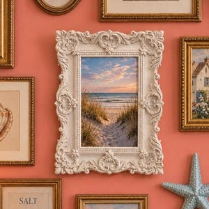 May include: A rectangular white picture frame with ornate, raised scrollwork and floral carvings. The frame contains a photograph of a sandy beach path leading to the ocean at sunset, with tall dune grasses on both sides under a soft, cloudy sky.